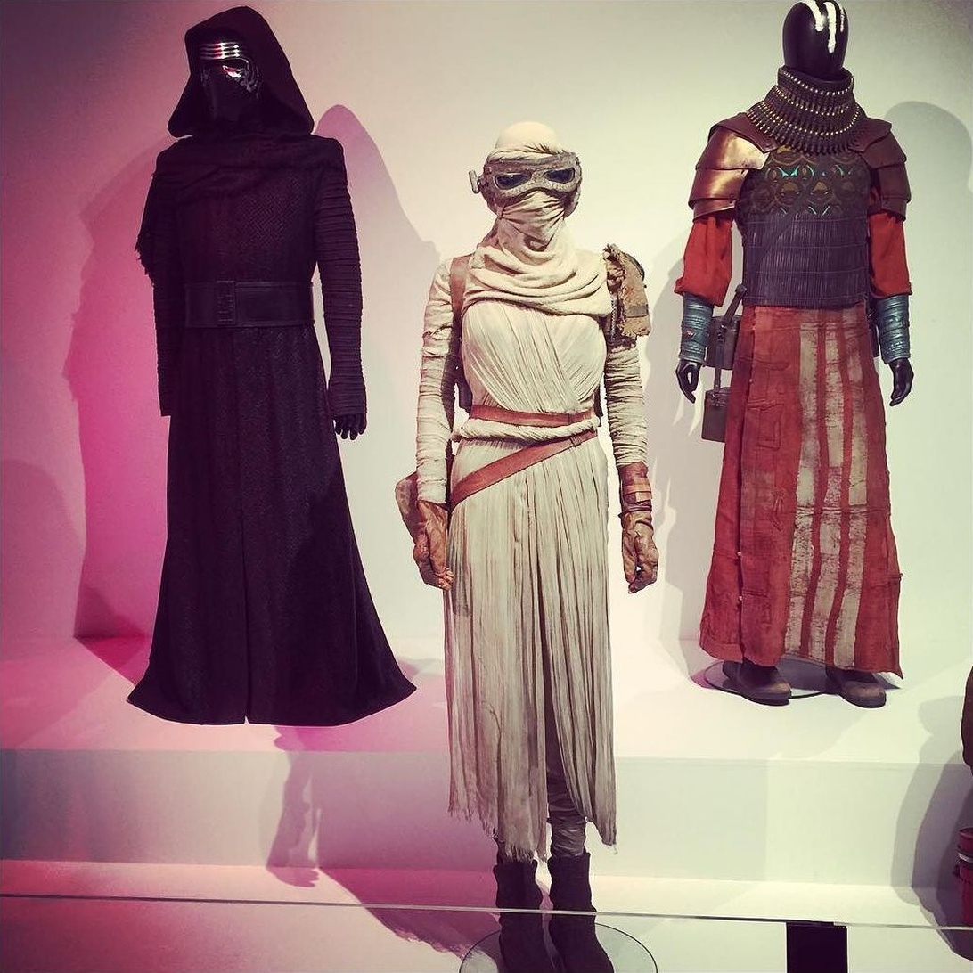 Drei ikonische Star-Wars-Filmkostüme in einer Museumsausstellung: Kylo Rens schwarze Robe, Reys Wüsten-Outfit und das Kostüm eines Ritters von Ren.